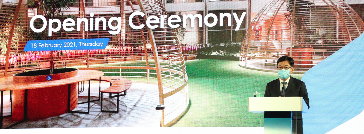 Man in suit and mask behind podium, overlaid "Opening Ceremony" and garden structure.